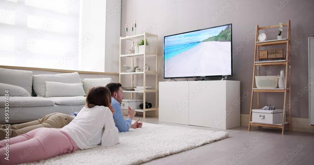 Young Couple Watching TV While Sitting On Sofa In Living Room Young Couple Watching TV While Sitting On Sofa In Living Room
