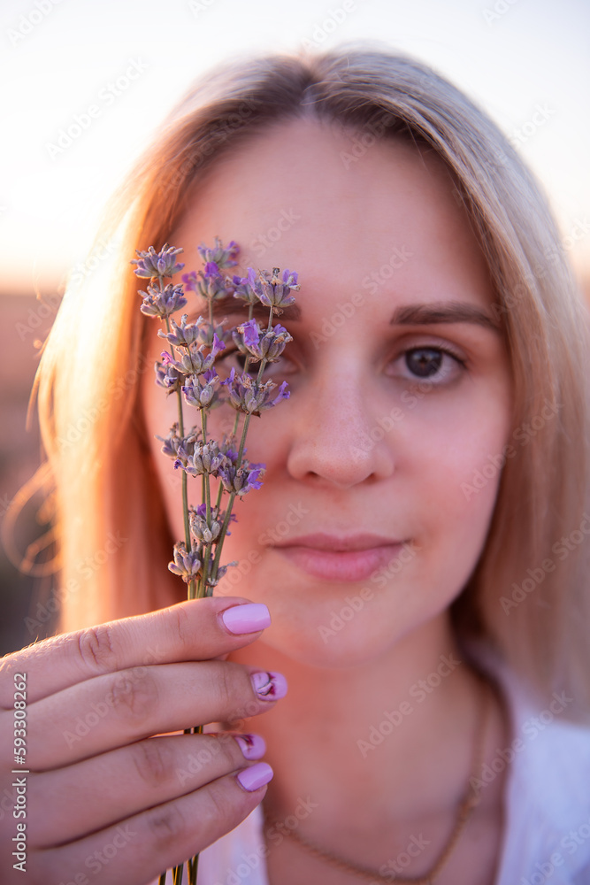 Sprigs purple lavender against background of blurred face of young blonde woman. Close-up portrait of millennial girl with clean skin without makeup. Allergy concept. Aroma oils, perfumery from nature