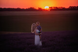 Millenial young mother holds little son in arms at sunset in purple lavender field. Walks in the countryside. Trust, protection of the child. Happy childhood. Allergy concept, single parent. Nature