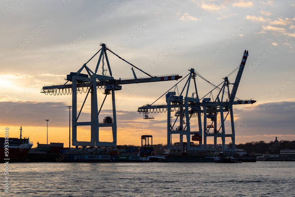 The busy harbour of Hamburg showing a skyline of cranes and container ships at sunset
