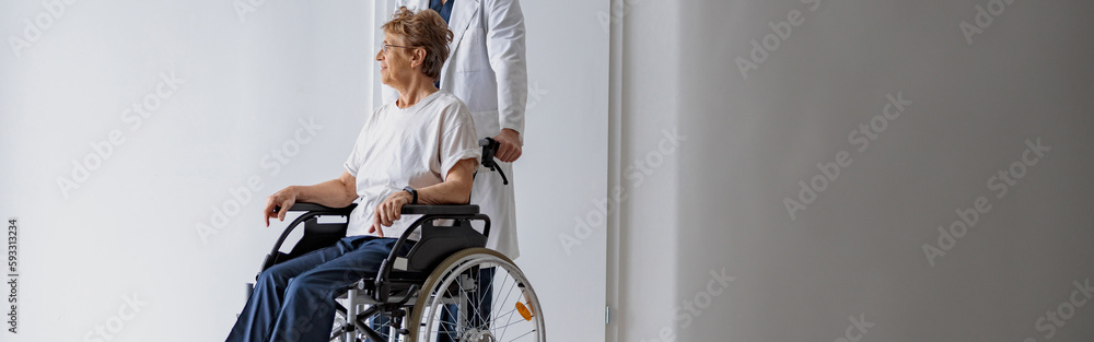 Professional male doctor carrying patient on wheelchair in medicine clinic hall. High quality photo Professional male doctor carrying patient on wheelchair in medicine clinic hall. High quality photo