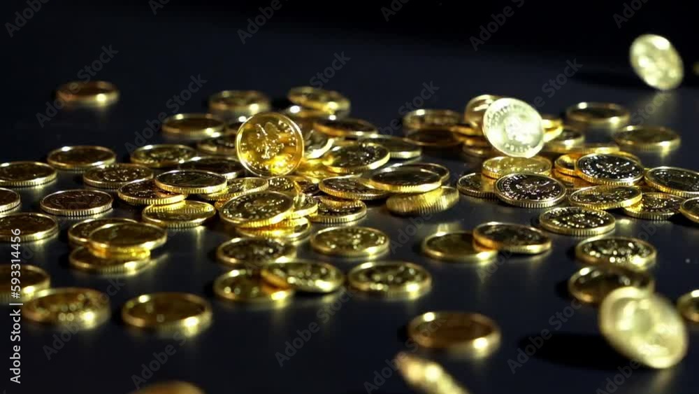 Slow motion of the golden coins falling on the black table surface on the blurred background Slow motion of the golden coins falling on the black table surface on the blurred background