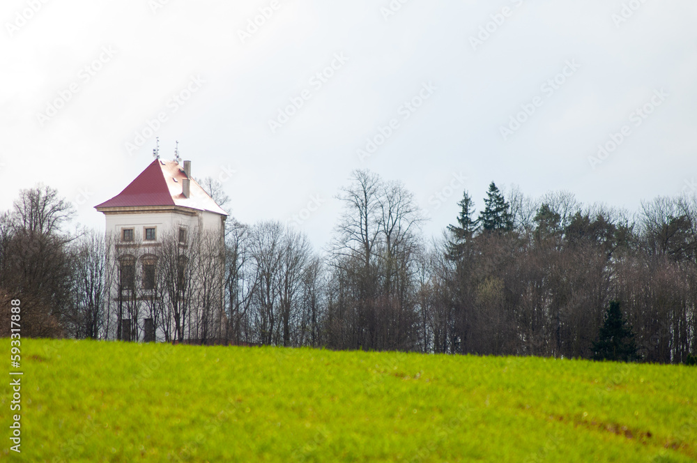 a white tower with a red roof on a hill behind a field and trees