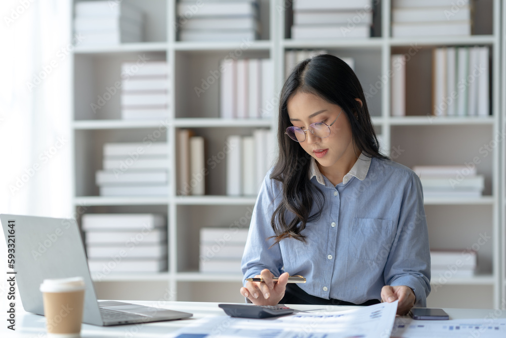 Young Asian businesswoman using a calculator to calculate business principles. Accounting statistics concept at the office. Young Asian businesswoman using a calculator to calculate business principles. Accounting statistics concept at the office.