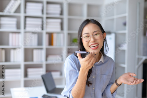 Happy beautiful smiling Asian businesswoman talking on mobile phone while working in office.