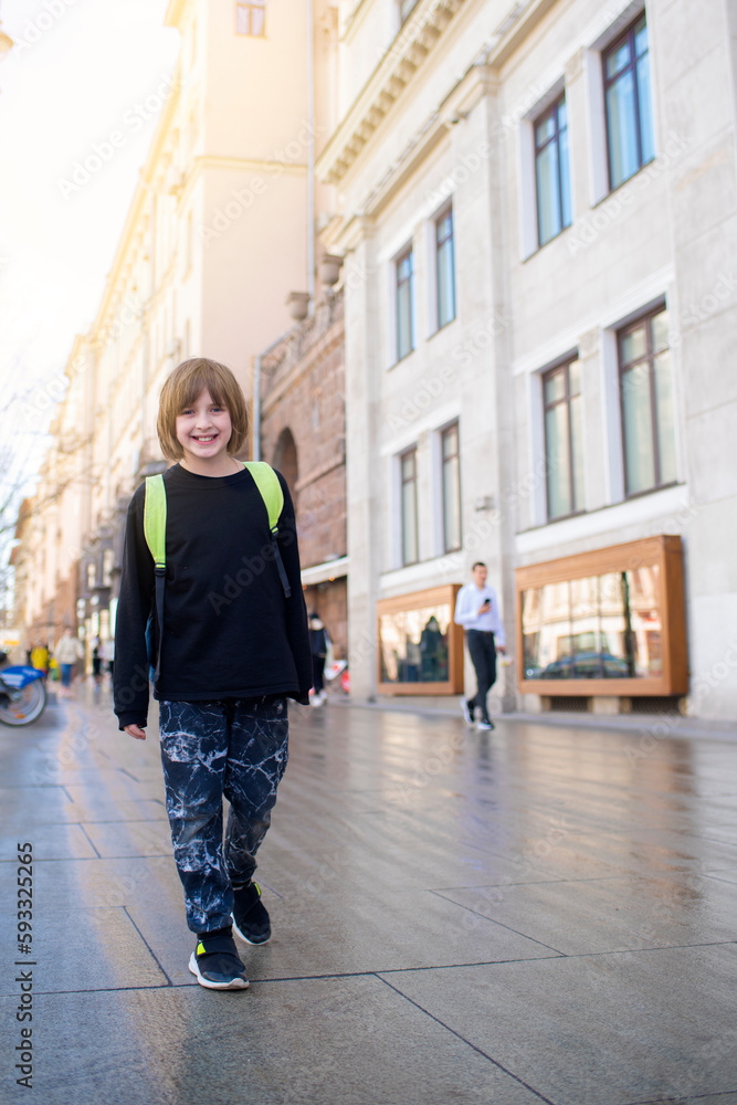 happy boy student in black clothes with a backpack walks around the city