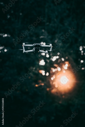 Selective focus of a drone in the air, sunlit trees blurred background
