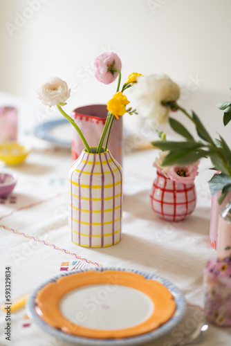 beautiful hand painted ceramic vases on set table with embroidered tablecloth filled with fresh ranunculus stems