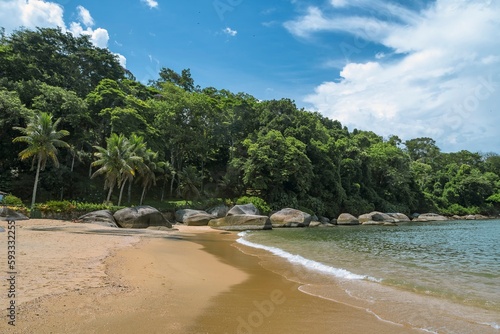 Natural landscape of Prainha in Paraty, Brazil. Sea in shades of turquoise blue, stones, strip of sand and blue sky with white clouds. In the background, the tropical forest..