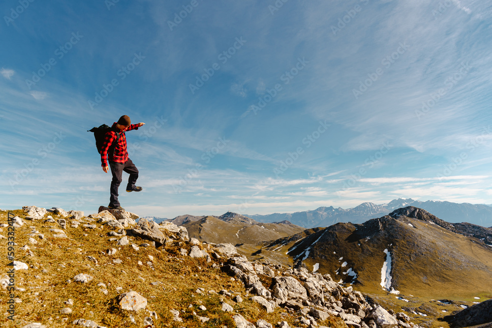 white male mountaineer with red clothes and backpack balancing on a rock on a mountain peak. lone hiker hiking a mountain trail on a sunny day. sport and adventure.