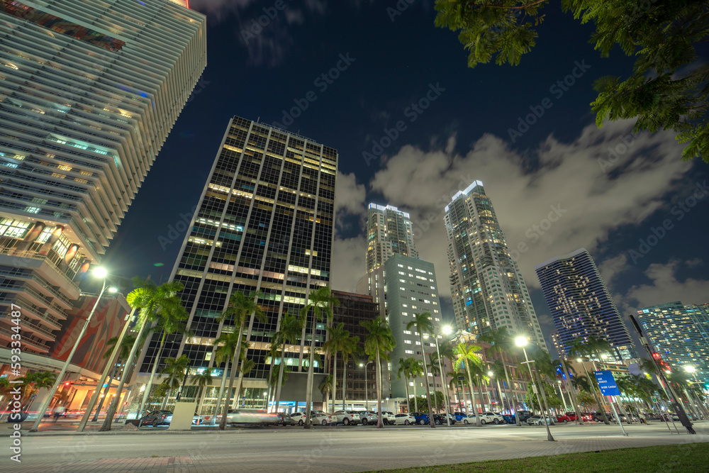 Downtown district of of Miami Brickell in Florida, USA. Brightly illuminated high skyscraper buildings and street with car trails and metrorail traffic in modern american midtown