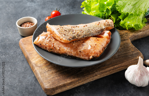 Raw salmon, greased with marinade with spices on a plate on a dark background with fresh herbs and vegetables. photo