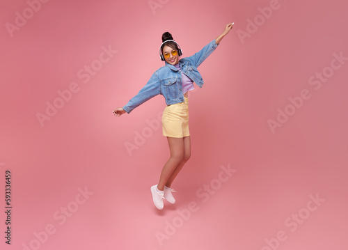 Full length happy asian teen woman wearing headphones listening to music and dancing on pink studio background. People lifestyle relax