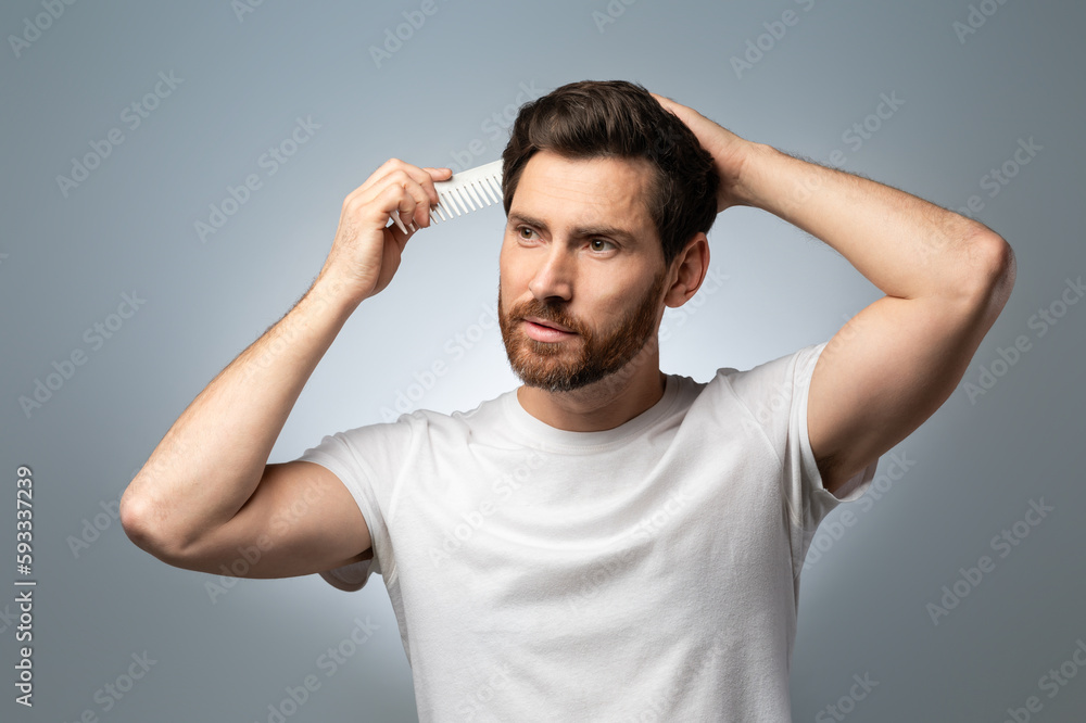 Barber shop concept. Handsome middle aged man in white t-shirt brushing his hair, standing over grey studio background Barber shop concept. Handsome middle aged man in white t-shirt brushing his hair, standing over grey studio background