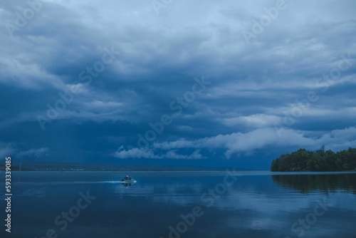Evening view of a blue sea with people on a small boat with mountains in the background © Mihai Constantin/Wirestock Creators