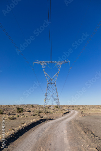 High voltage electricity transmission pylons and lines with a gravel road next to it in the Karoo area of South Africa