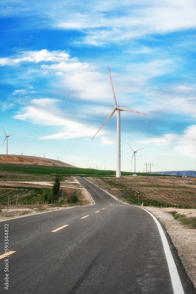 Vertical shot of an open road in the middle of an agricultural field with wind turbines
