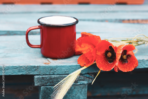 Still Life with a red coffee or tea cup and a bouquet of red poppies on a wooden blue surface. Gathering wild spring flowers in a garden. Rural scene. Vintage retro spring nature background. Nostalgia
