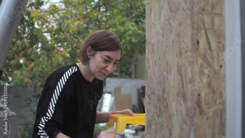Woman worker covers the corner of her own wooden house with primer. Hand with brush