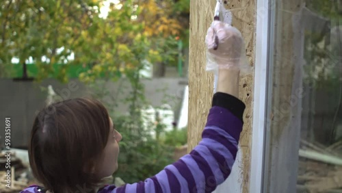 Beautiful woman worker paints slopes of windows of her own wooden house. Hand with brush