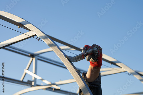 A man's hand paints the frame of a greenhouse with a paintbrush against a bright blue sky. Copy space.