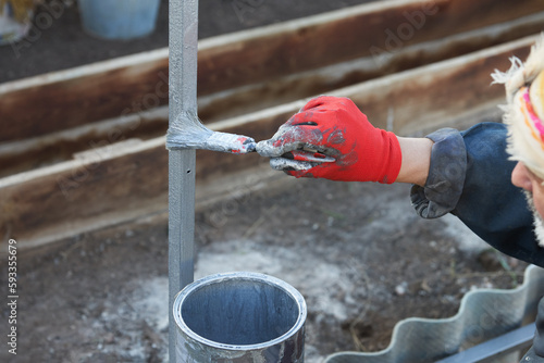 A man paints the frame of a greenhouse with a brush with anti-corrosion paint.