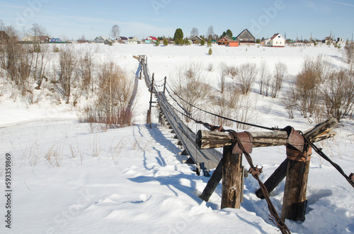 Wooden suspension bridge in the northern village. Village landscape in spring