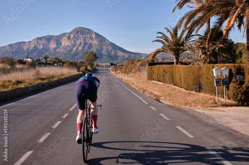 Pushing the Limits: A Fit Cyclist on Time Trial Aero Bike Rides towards the Mountains in the Aero Position on an Empty Road. Get motivated and stay on track concept photo.
