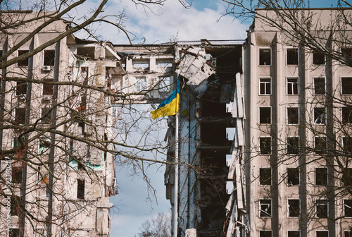 Flag of Ukraine against the background of a destroyed building in Ukraine. The building was destroyed by a Russian air bomb
