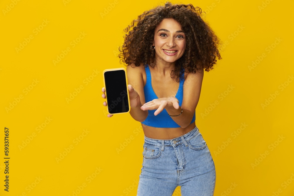 Influencer woman with phone in hand taking selfies talking on video call freelancer social media technology work, with curly afro hair in blue shirt yellow background , smile with teeth, copy space Influencer woman with phone in hand taking selfies talking on video call freelancer social media technology work, with curly afro hair in blue shirt yellow background , smile with teeth, copy space