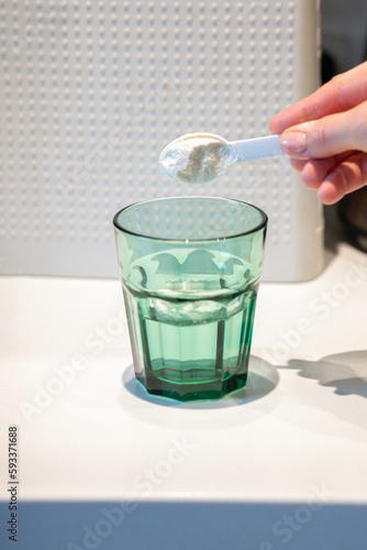 Woman's hand pours white powder with medicine into transparent glass of water with spoon. High quality photo