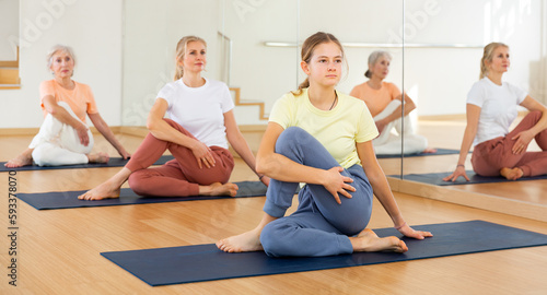 Portrait of active woman practicing yoga in group, making twisting asana