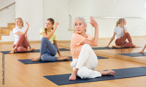 Senior woman practicing lord of fishes pose with her daughter and granddaughter during yoga training in studio.