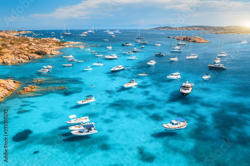 Aerial view of luxury yachts on blue sea at sunset in summer. Sardinia, Italy. Aerial view of speed boats, yachts, sea lagoon, shore, transparent water, sky. Top view from drone. Tropical seascape
