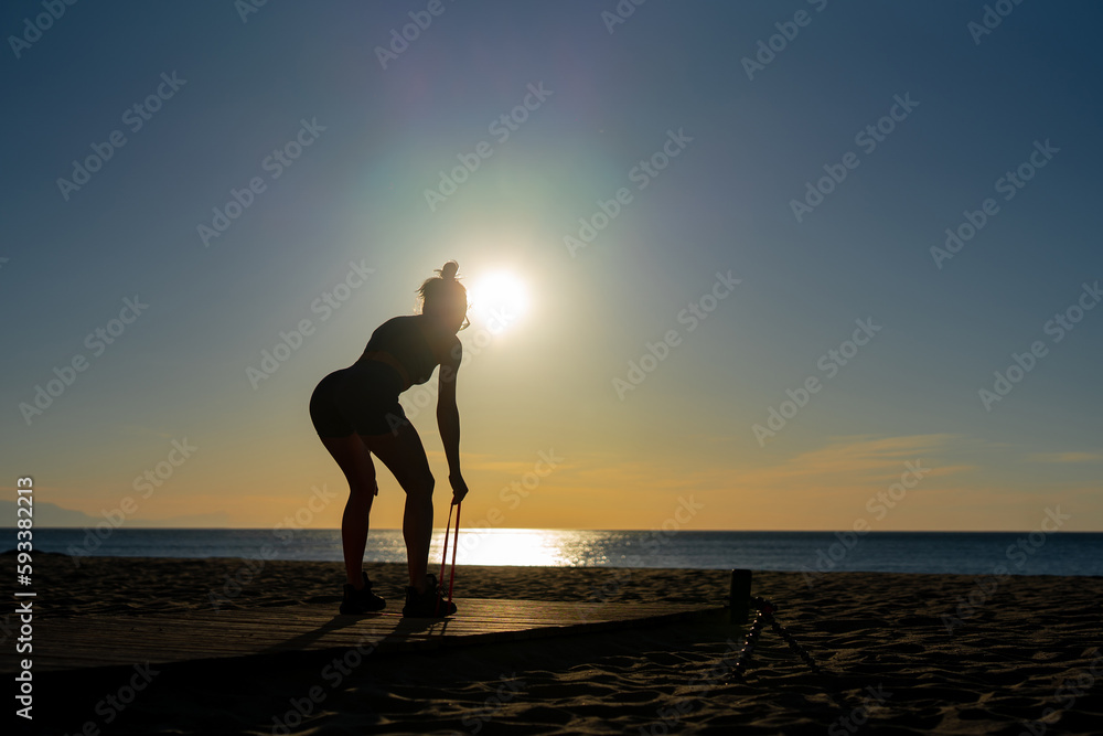 beautiful girl goes in for sports doing exercises with an expander on the seashore at dawn