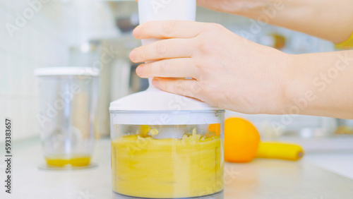 Obraz na płótnie In a kitchen, a young woman prepares a healthy smoothie using a blender. Surrounding her are fresh fruits, including sliced pineapple on a wooden cutting board. nutrition and healthy eating. w salonie