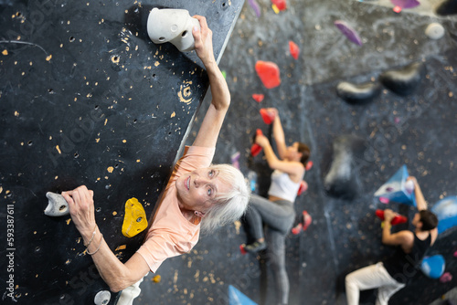 elderly slender muscular athlete climbed to top of artificial black bouldering wall.Top view