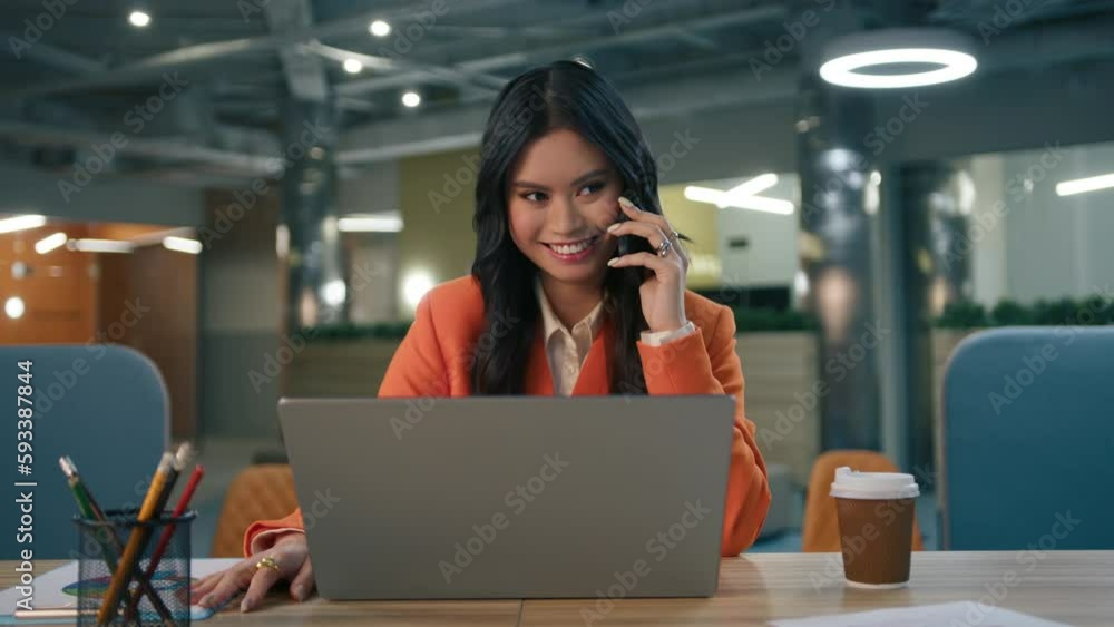 Excited young Asian American business lady enjoying successful work project at office. Ethnical woman sitting at desk with opened laptop, talking by smartphone, having fun celebrating good news slowmo Excited young Asian American business lady enjoying successful work project at office. Ethnical woman sitting at desk with opened laptop, talking by smartphone, having fun celebrating good news slowmo