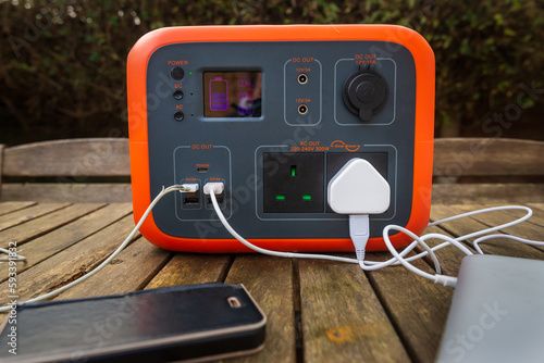 Portable power station solar electricity generator on table with mobile phone and laptop charging.