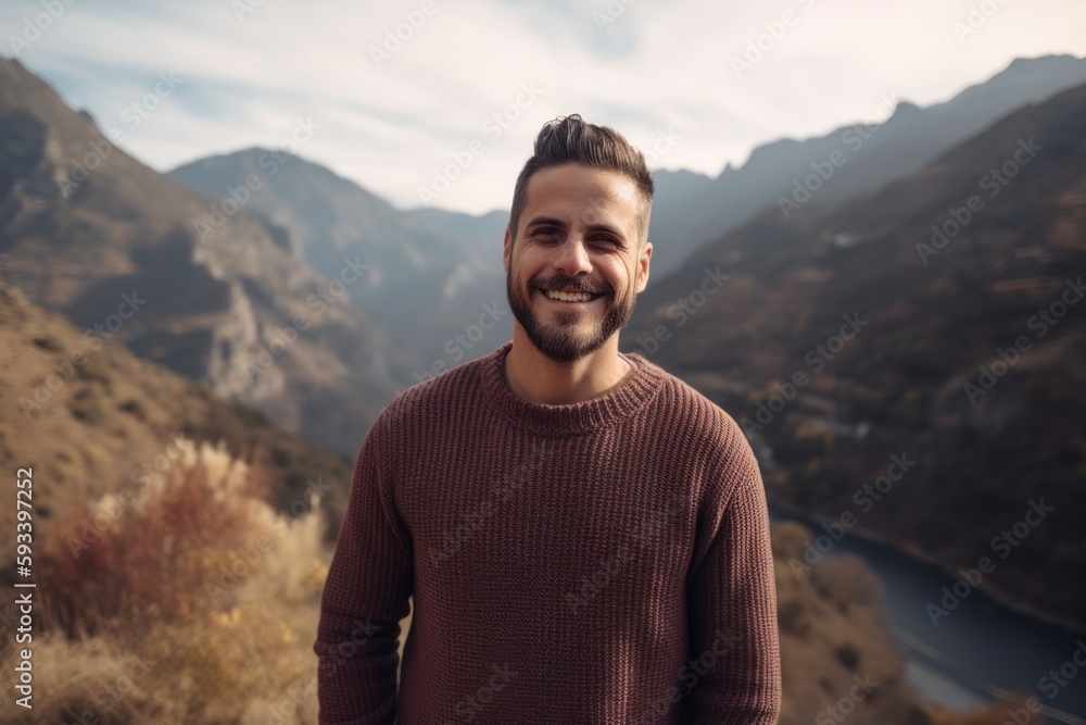 Portrait of a handsome young man with a beard smiling at the camera in the mountains