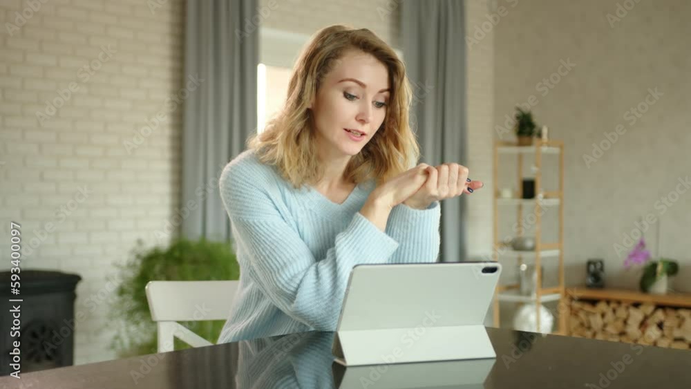Attractive young woman is holding online conversation at home with cozy interior using tablet in white cover. The blonde behaves friendly. Tablet on table. High quality 4k footage Attractive young woman is holding online conversation at home with cozy interior using tablet in white cover. The blonde behaves friendly. Tablet on table. High quality 4k footage