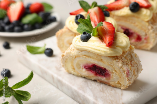 Tasty meringue roll with jam, cream, strawberry, blueberry and mint on table, closeup