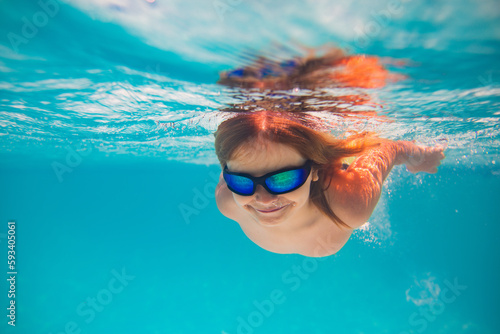 Child dives into the water in swimming pool. little kid swim underwater in pool. Child swimming underwater in sea or pool water. Summer vacation fun. Underwater portrait cute kid in swimming pool. © Volodymyr