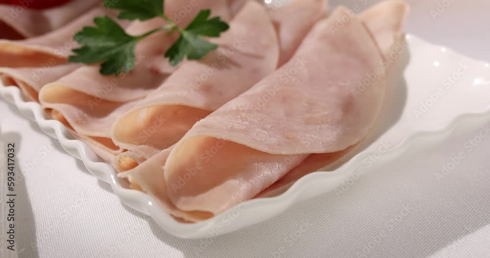 ham on a plate. meat delicacy with cherry tomato on a light background. turkey ham slices with parsley. cold appetizer on a white tablecloth. treat close-up. ham on a plate. meat delicacy with cherry tomato on a light background. turkey ham slices with parsley. cold appetizer on a white tablecloth. treat close-up.