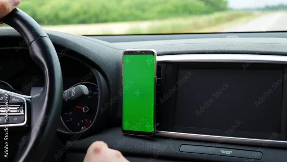 Driver controlling car and using smartphone with empty green screen. Searching location via gps navigator application. Concept for communication technology. Driver controlling car and using smartphone with empty green screen. Searching location via gps navigator application. Concept for communication technology.