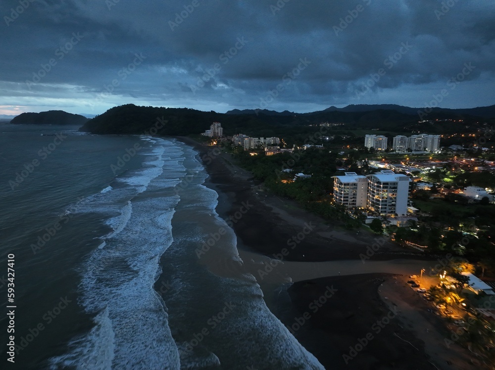 Glimmering lights, bustling activity, and serene waves characterize Jaco Beach's nighttime drone images.