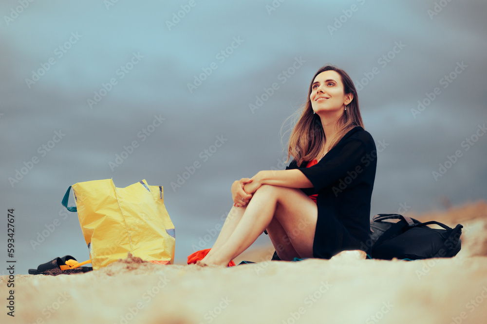 Happy Woman Sitting on a Towel at the Beach. Cheerful girl enjoying a peaceful summer vacation at the seaside
