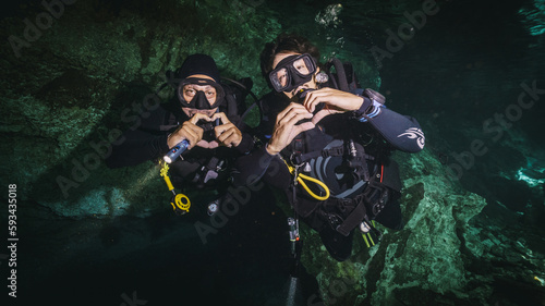 TWO DIVERS DOING HEARTS WITH THE HANDS IN A CENOTE