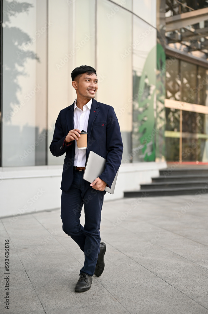 Portrait of a confident Asian businessman walking in a city with his takeaway coffee and laptop. Portrait of a confident Asian businessman walking in a city with his takeaway coffee and laptop.