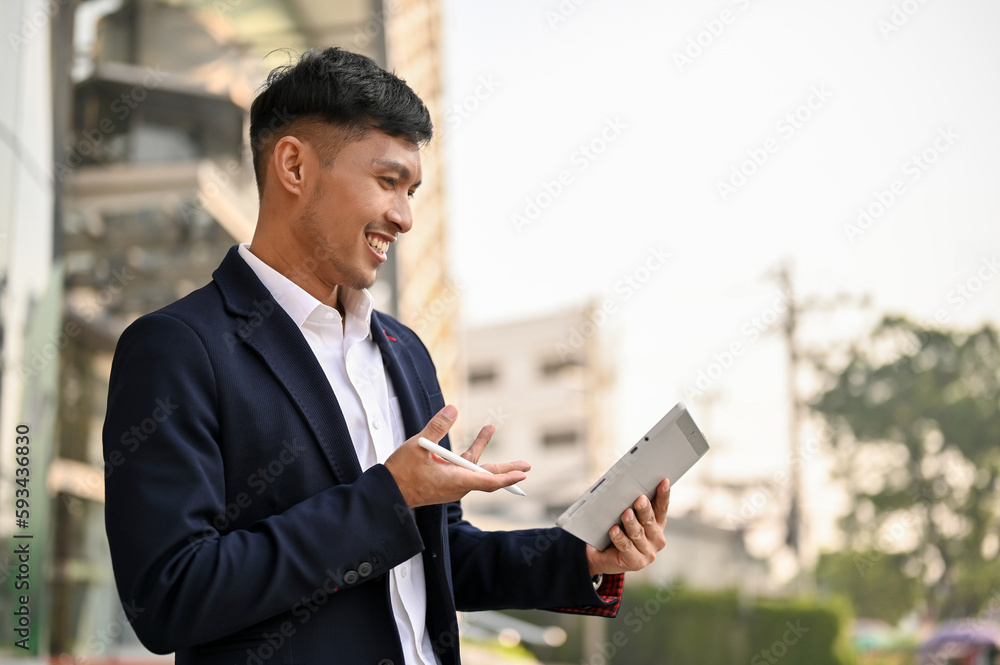 An Asian businessman video calling with his team via tablet while walking in a city.